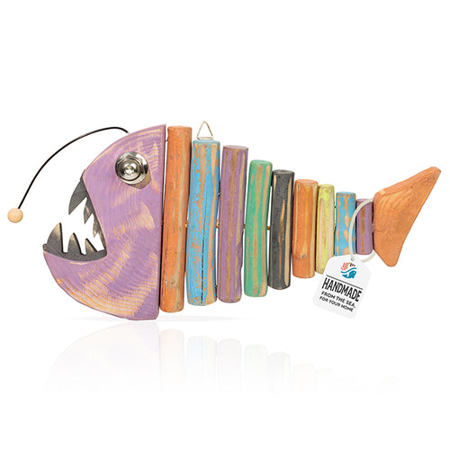 Handcrafted wooden fish wall art featuring a purple-painted head with stylized teeth and body segments made of various colorful driftwood-style pieces, including a tag that reads "Handmade From The Sea For Your Home."